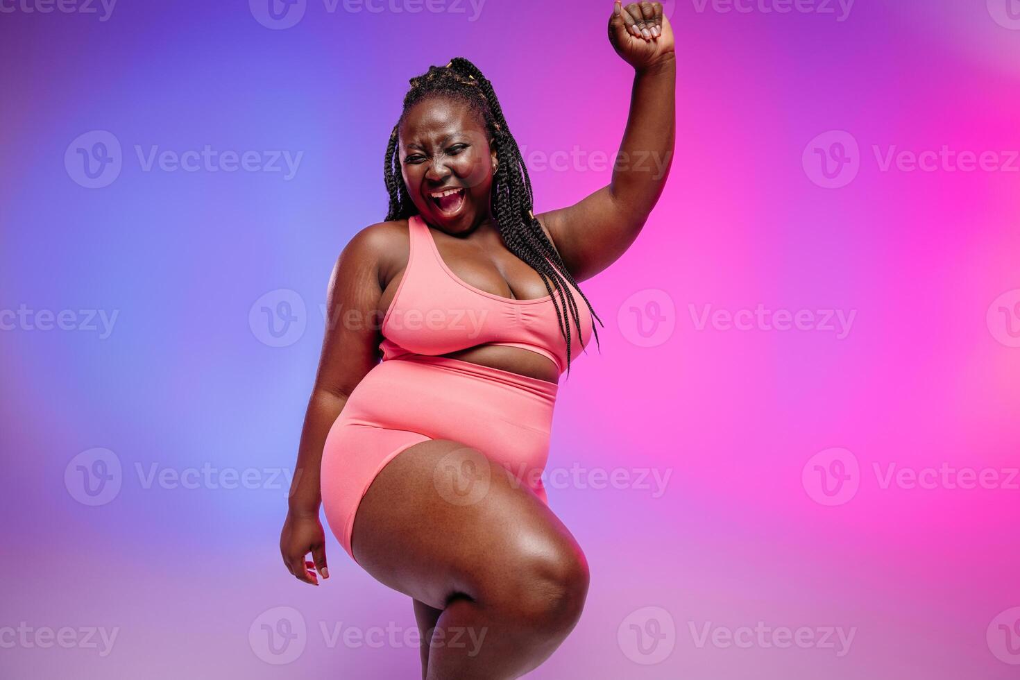 Beautiful plus size woman in sportswear radiating love to her body while dancing on vibrant background photo