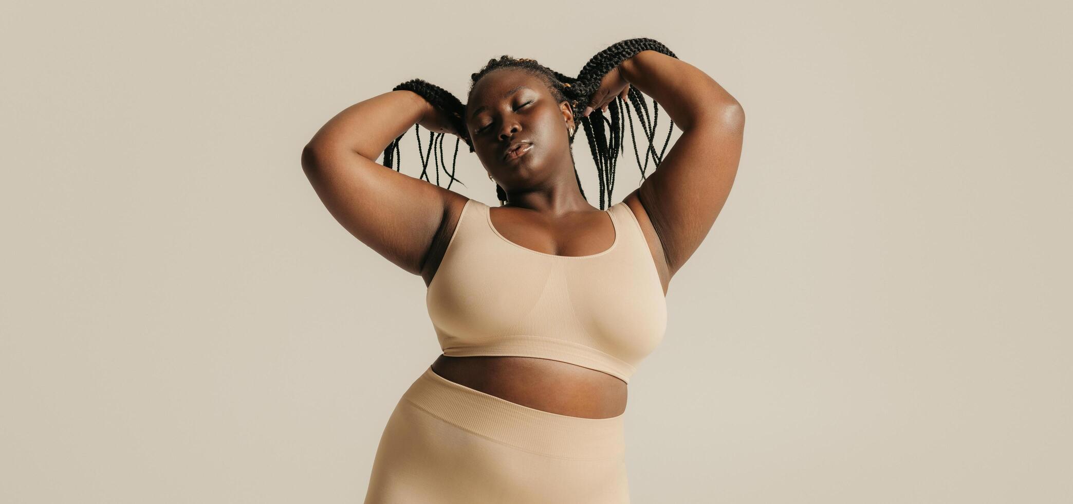 Calm African plus size woman in underwear radiating self-love while standing on studio background photo