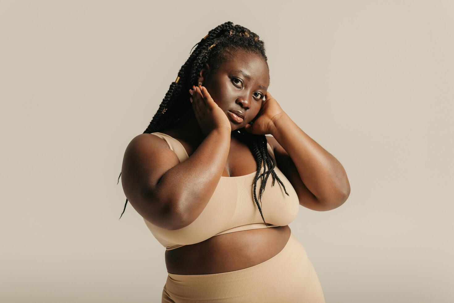 Beautiful curvy African woman in underwear touching face and looking at camera on studio background photo