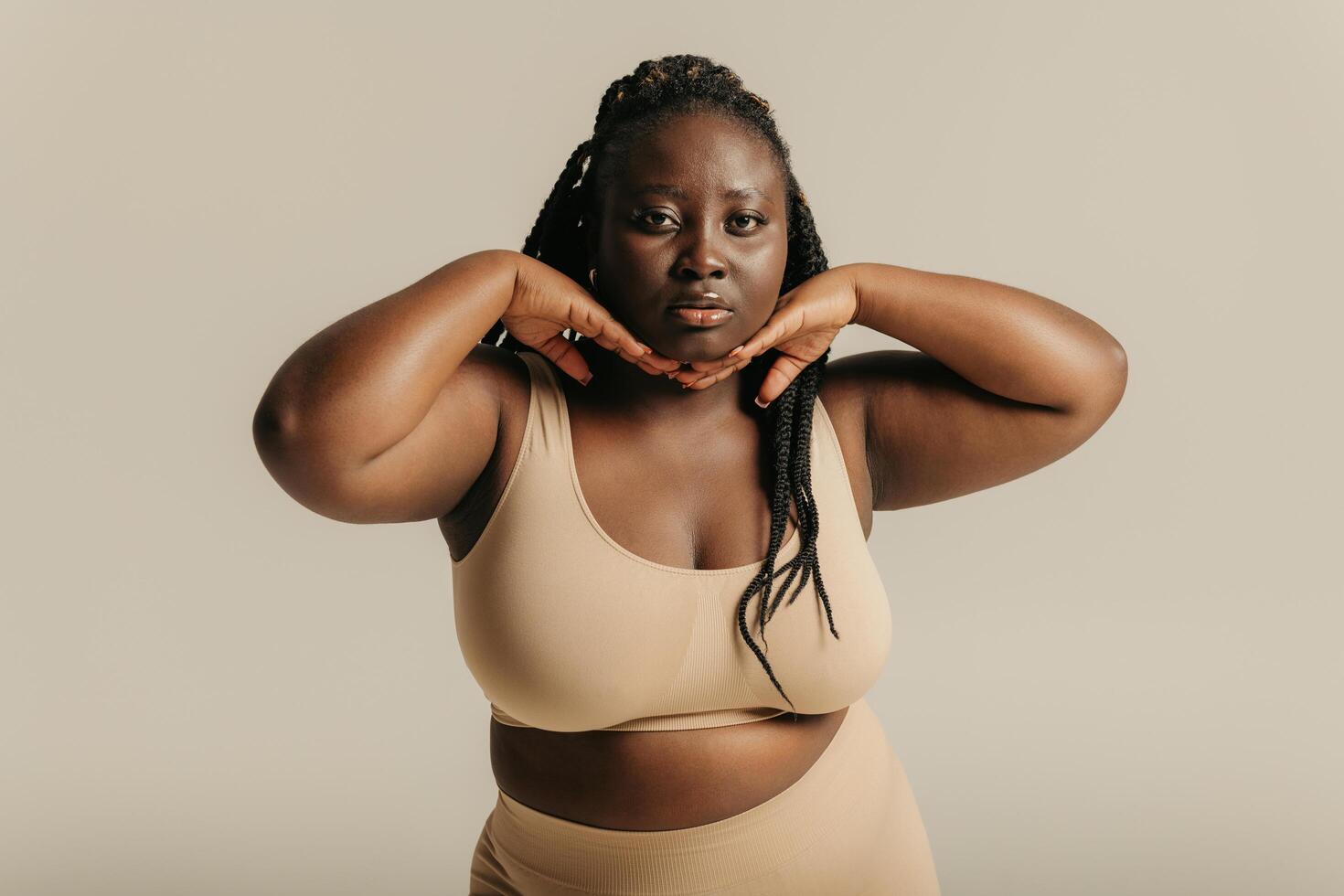 Beautiful curvy African woman in underwear touching face and looking at camera on studio background photo