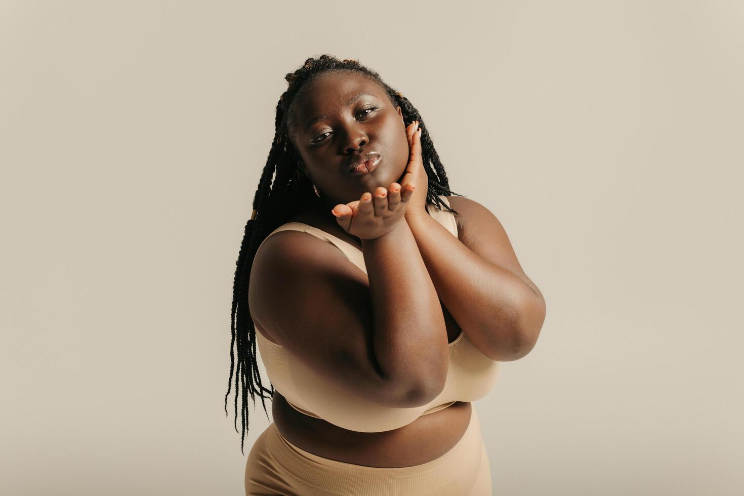 Beautiful voluptuous African woman in underwear touching face and smiling on studio background photo