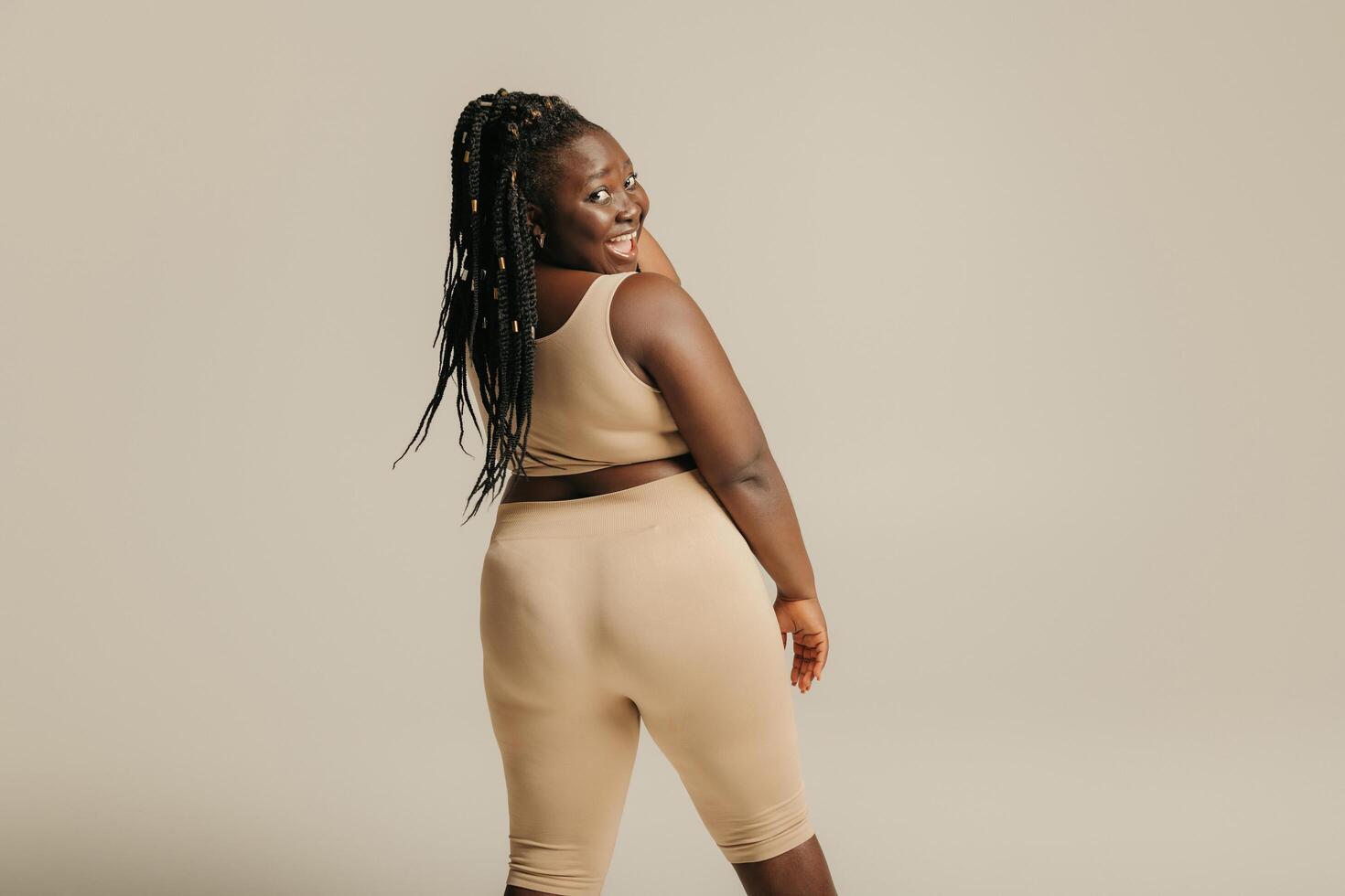 Rear view of happy curvy African woman in sportswear looking over shoulder on studio background photo