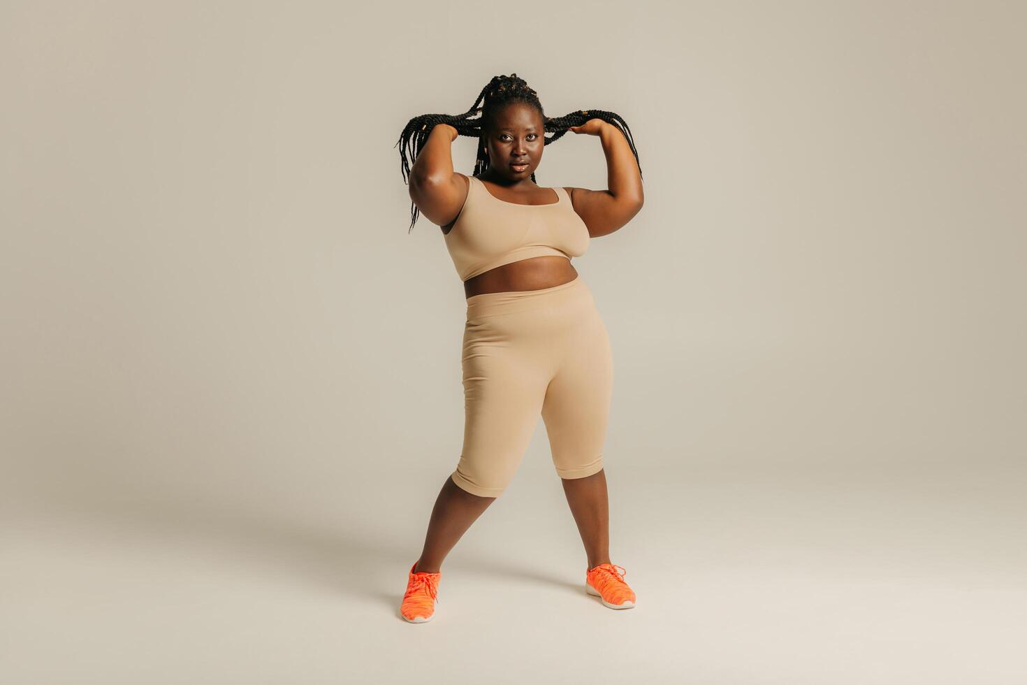 Full Length of beautiful African plus size woman in sportswear adjusting her dreadlocs on studio background photo