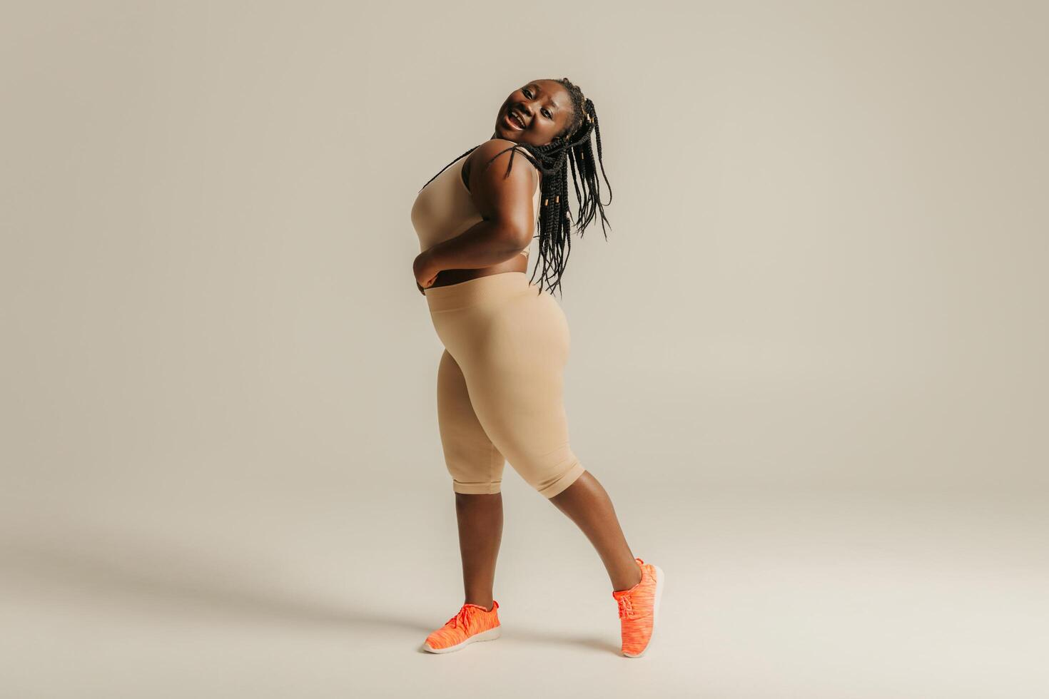 Happy plus size African woman in sportswear looking confident in her body while standing on studio background photo