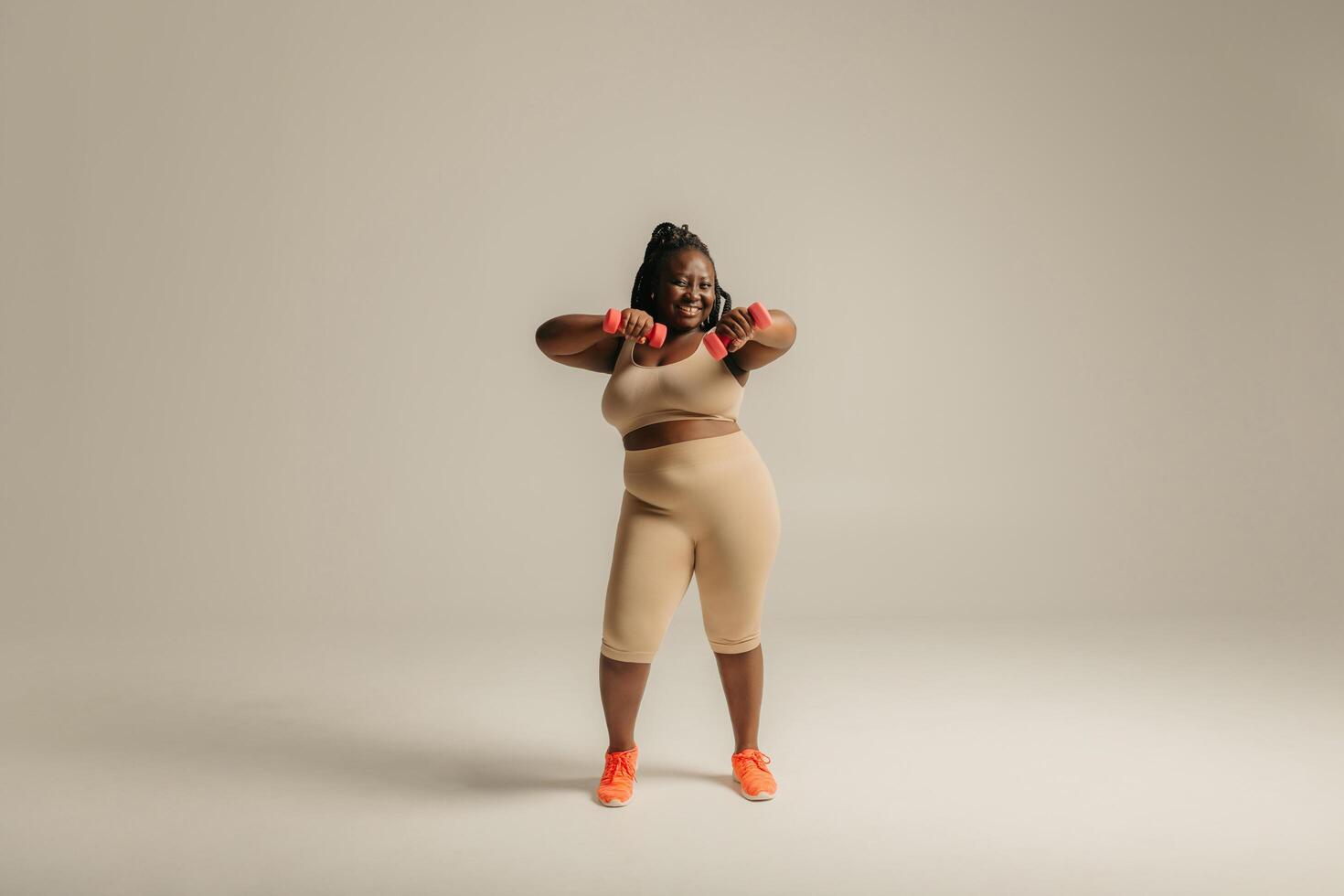 Full length happy plus size African woman in sportswear exercising with dumbbells on studio background photo