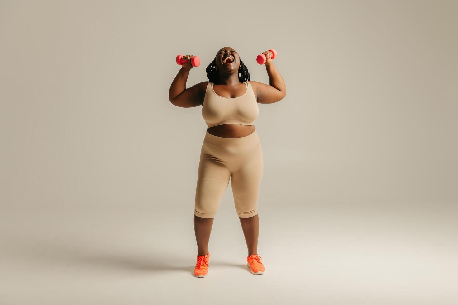 Full length joyful plus size African woman in sportswear exercising with dumbbells on studio background photo