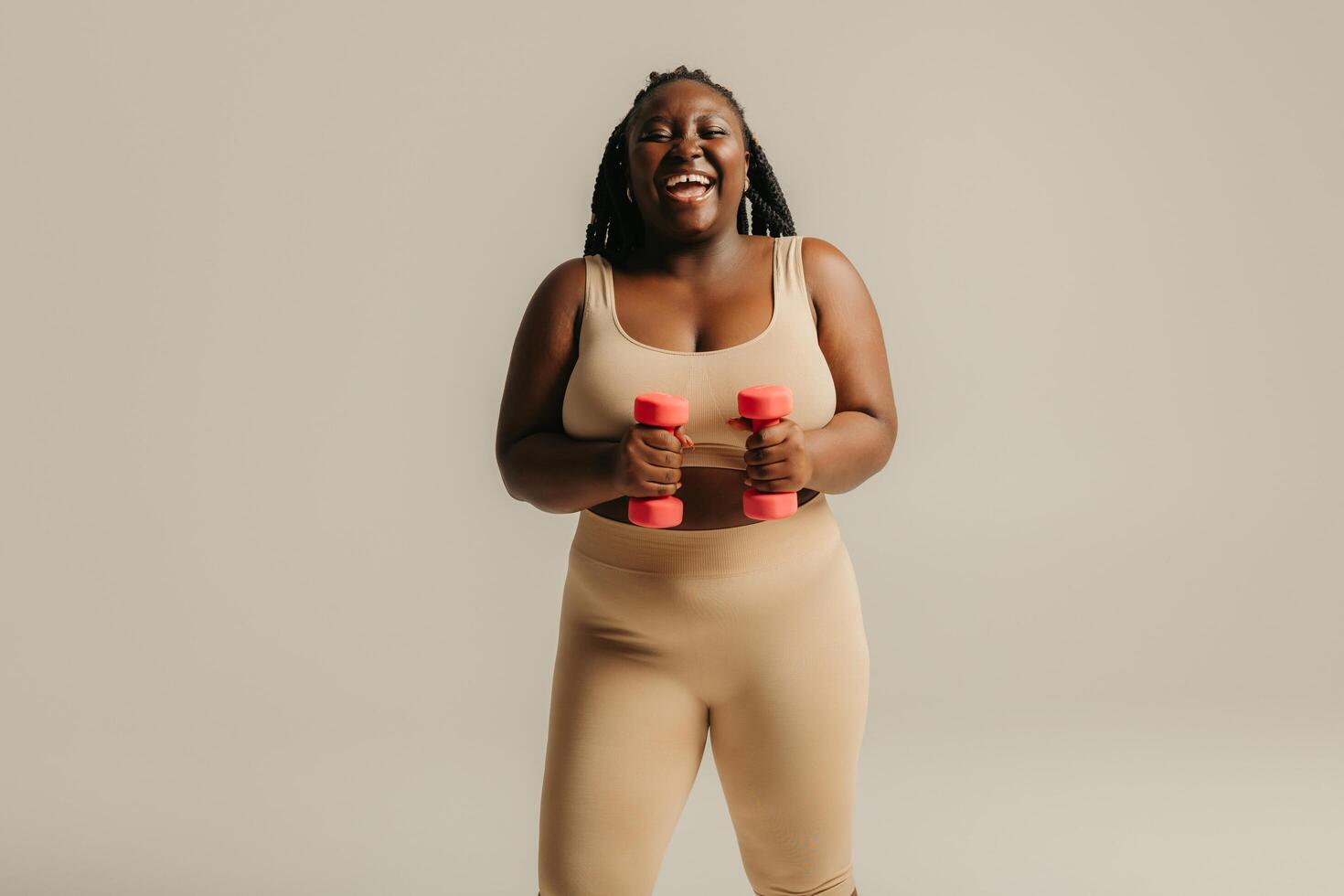Happy plus size African woman in sportswear exercising with dumbbells on studio background photo