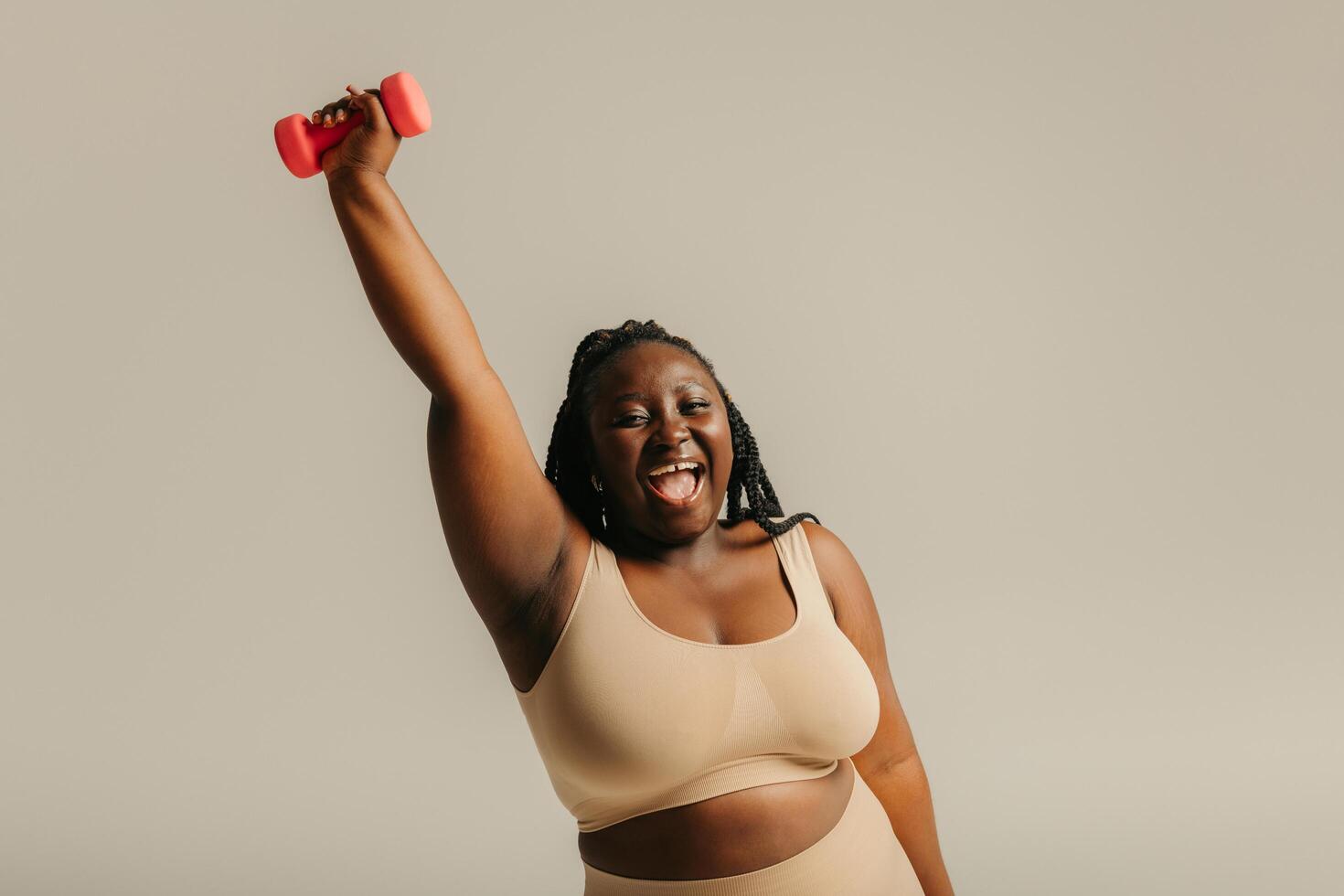 Joyful plus size African woman in sportswear exercising with dumbbell on studio background photo