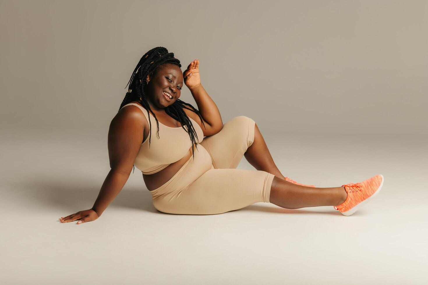 Joyful plus curvy African woman in sportswear radiating self-love while sitting against studio background photo
