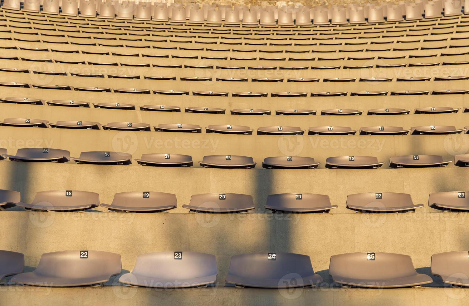Rows of empty stadium seats, numbers visible, sunlight casting shadows, concert or sports event venue concept photo