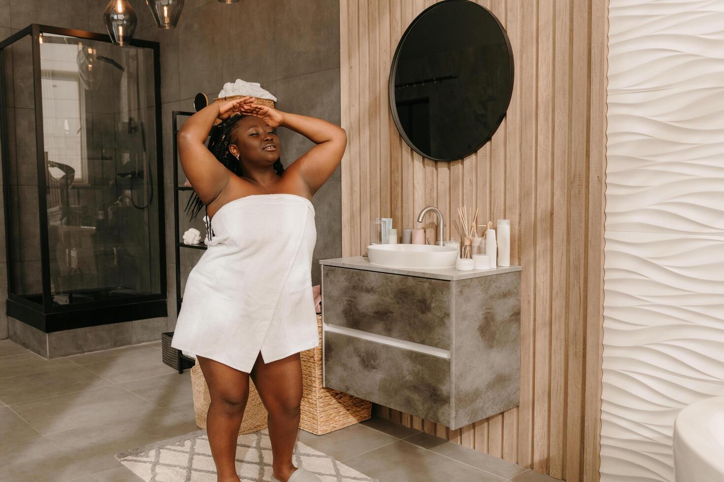 Beautiful plus size African woman covered in towel enjoying time in domestic bathroom photo