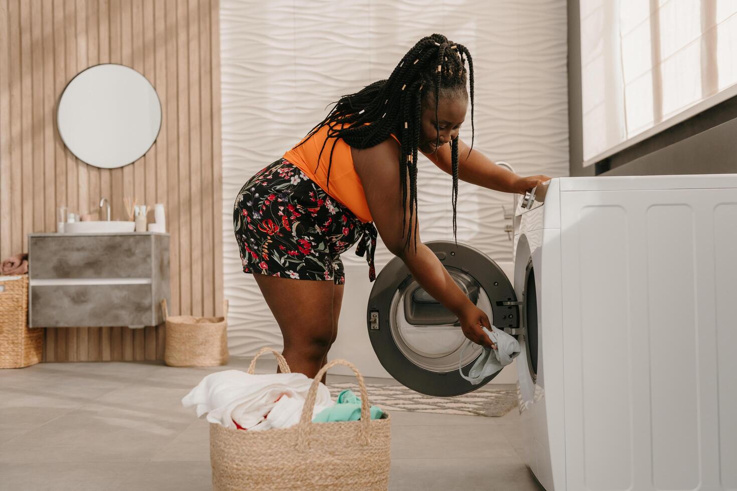 Beautiful curvy African woman loading clothes into washing machine while standing in bathroom photo