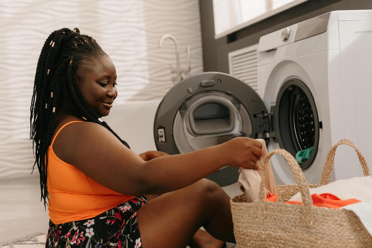 Happy plus size African woman merchandizing fresh and clean clothes near the washing machine in bathroom photo