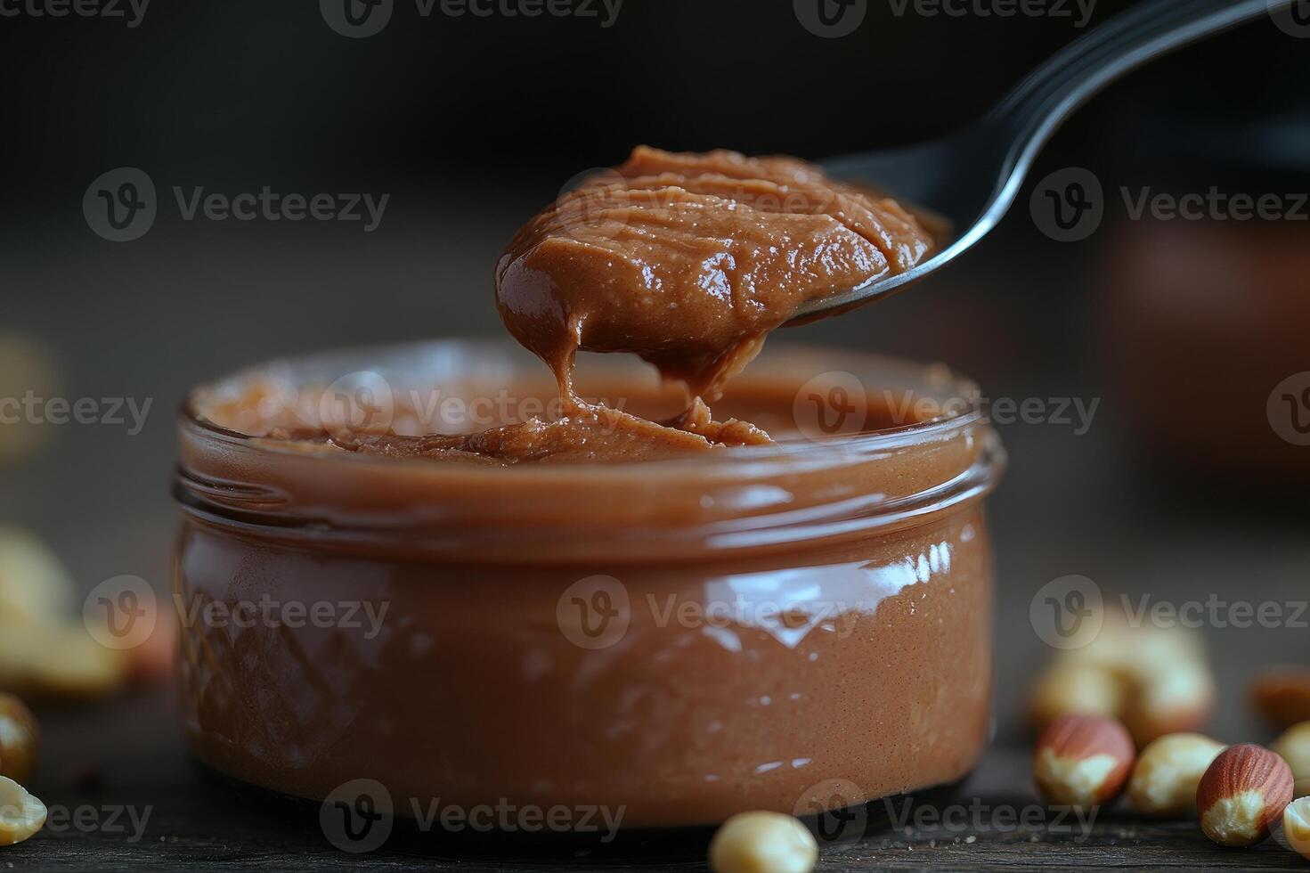 Spoon scooping creamy peanut butter from jar surrounded by peanuts photo