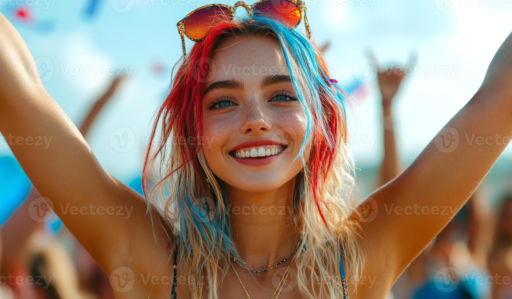A woman with blue, red, and white hair is smiling and holding her arms up in the air photo