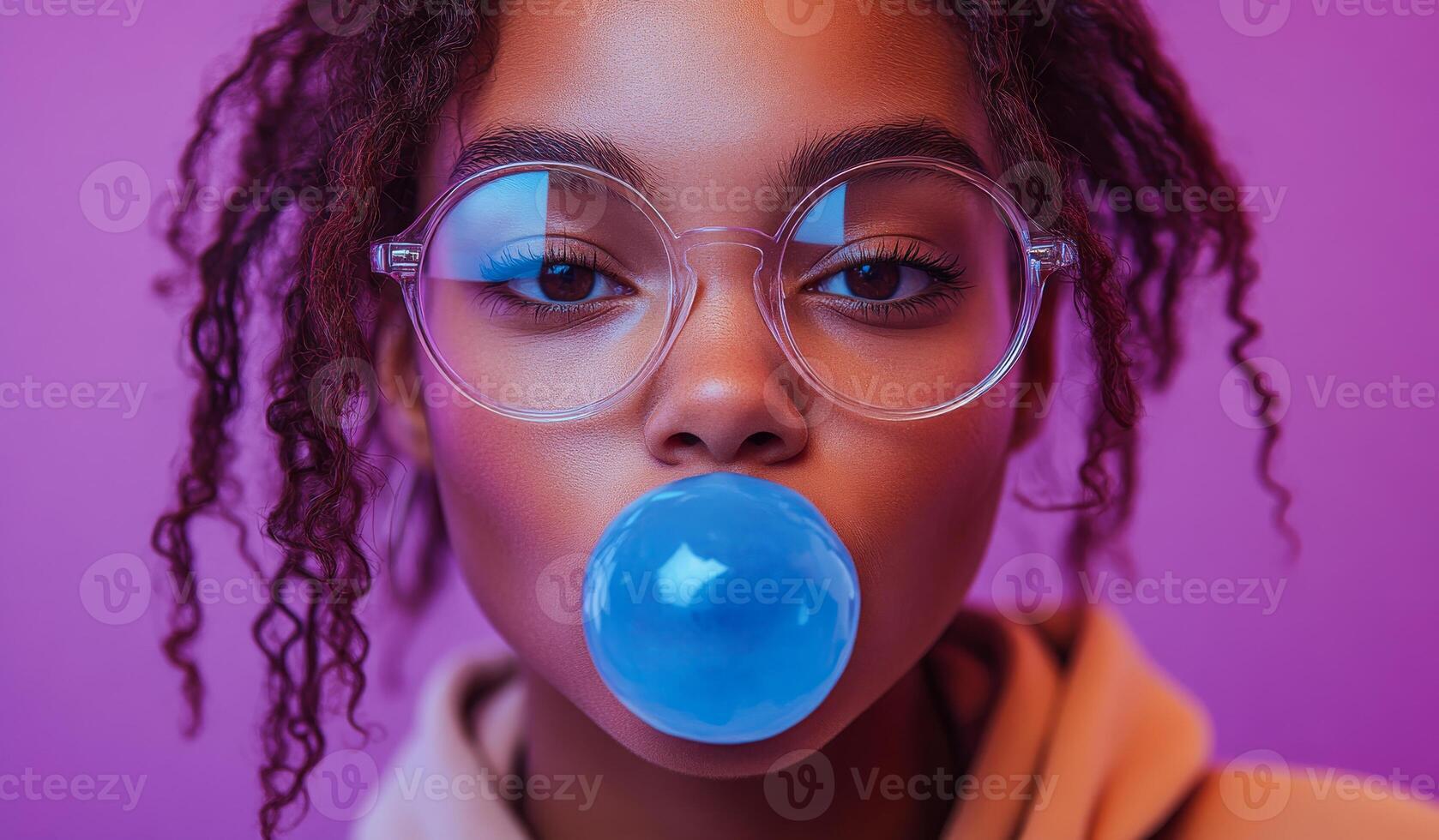 A woman with curly hair is blowing bubbles with a blue bubblegum. The image has a fun and playful mood, as the woman is enjoying a simple and lighthearted activity photo