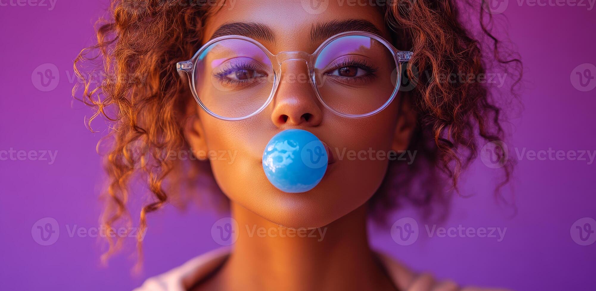 A woman with curly hair is blowing bubbles with a blue bubblegum. The image has a fun and playful mood, as the woman is enjoying a simple and lighthearted activity photo