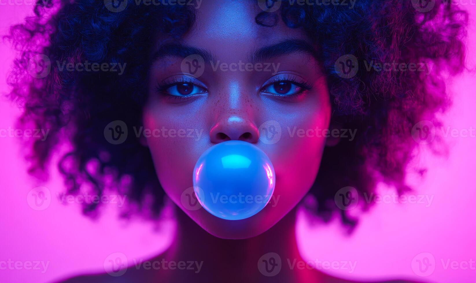 A woman with curly hair is blowing bubbles. The bubbles are blue and the woman is looking at the camera. The image has a fun and playful mood photo