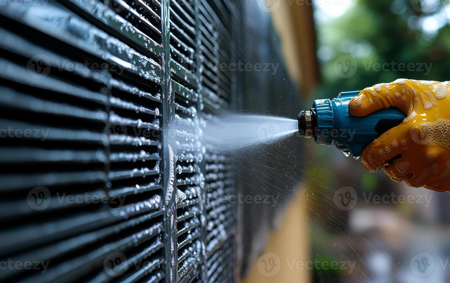A person is spraying water on a wall. The wall is covered in black tiles. The person is wearing a yellow glove photo