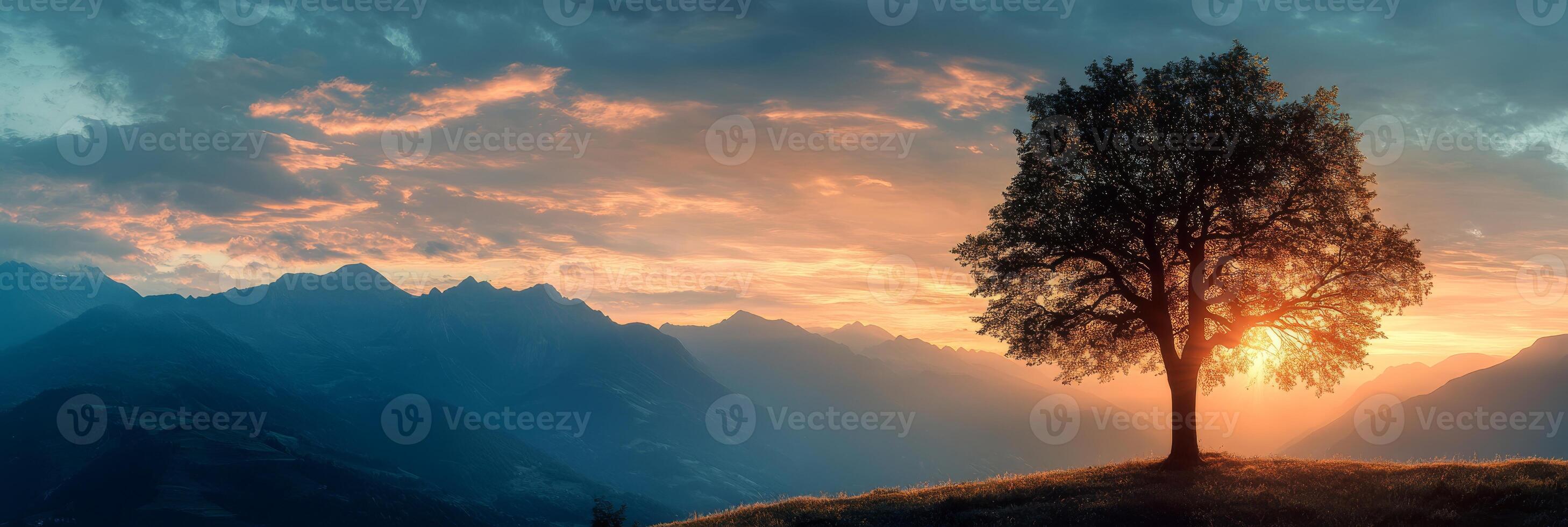 A breathtaking sunset illuminates the landscape, casting stunning golden hues gently over the majestic mountains, with a solitary, elegant tree beautifully silhouetted against the vibrant evening sky photo