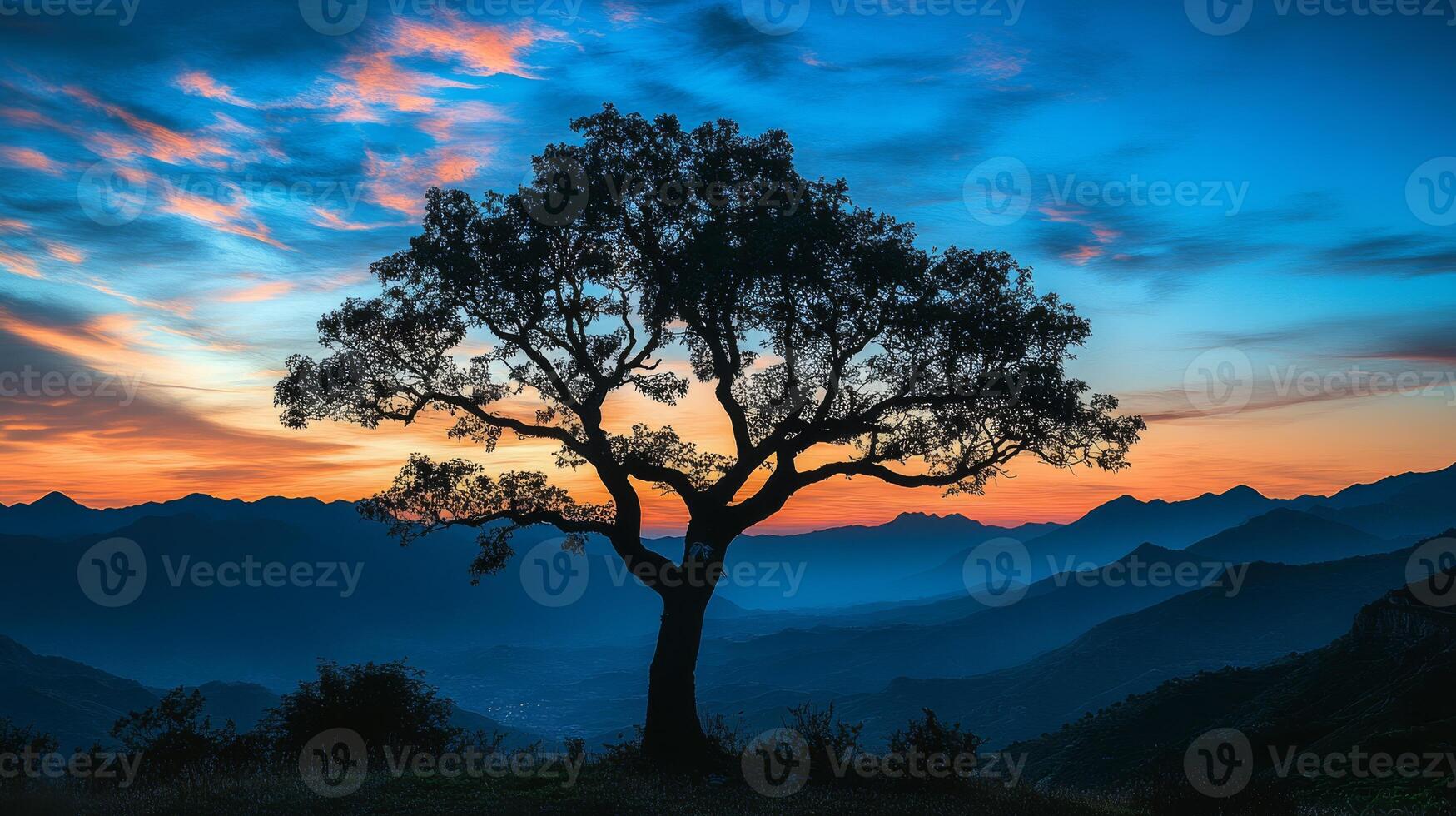A beautiful silhouette of a majestic tree stands against a sunset, framed by distant mountains and clouds, creating a peaceful atmosphere that captivates the soul and invites reflection photo
