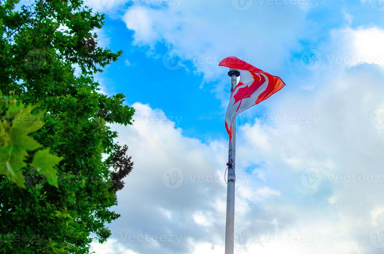 Canadian Flag Waving on Flagpole Against Blue Sky with Clouds photo