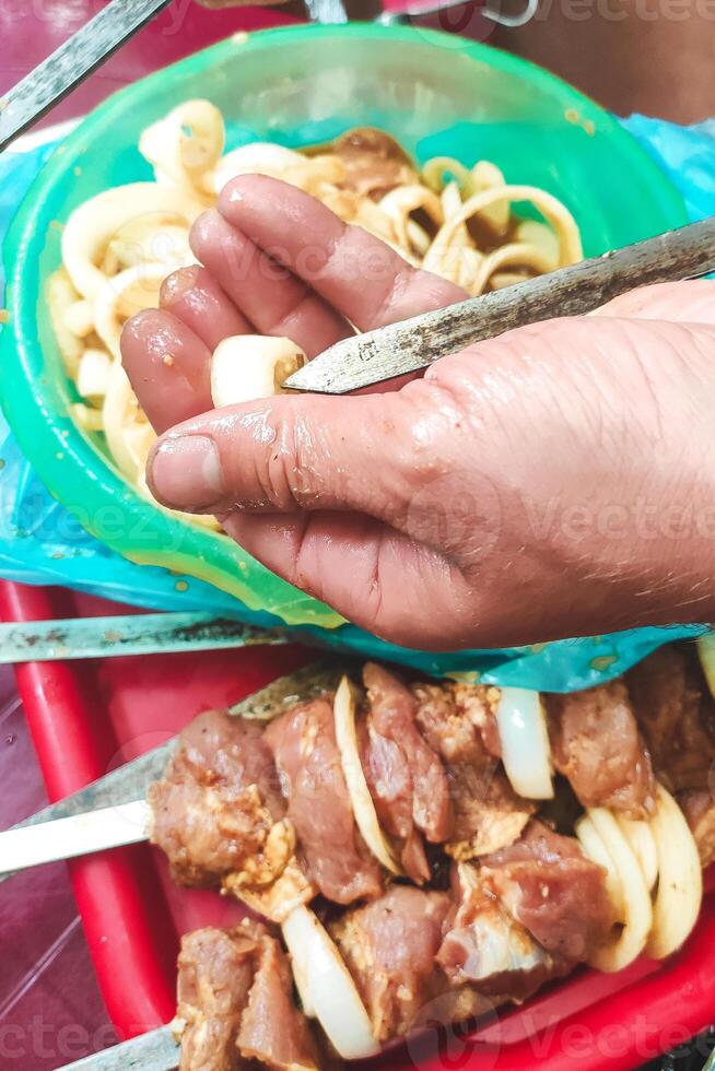 a man's hand stringing gray meat on a skewer to fry a kebab. photo