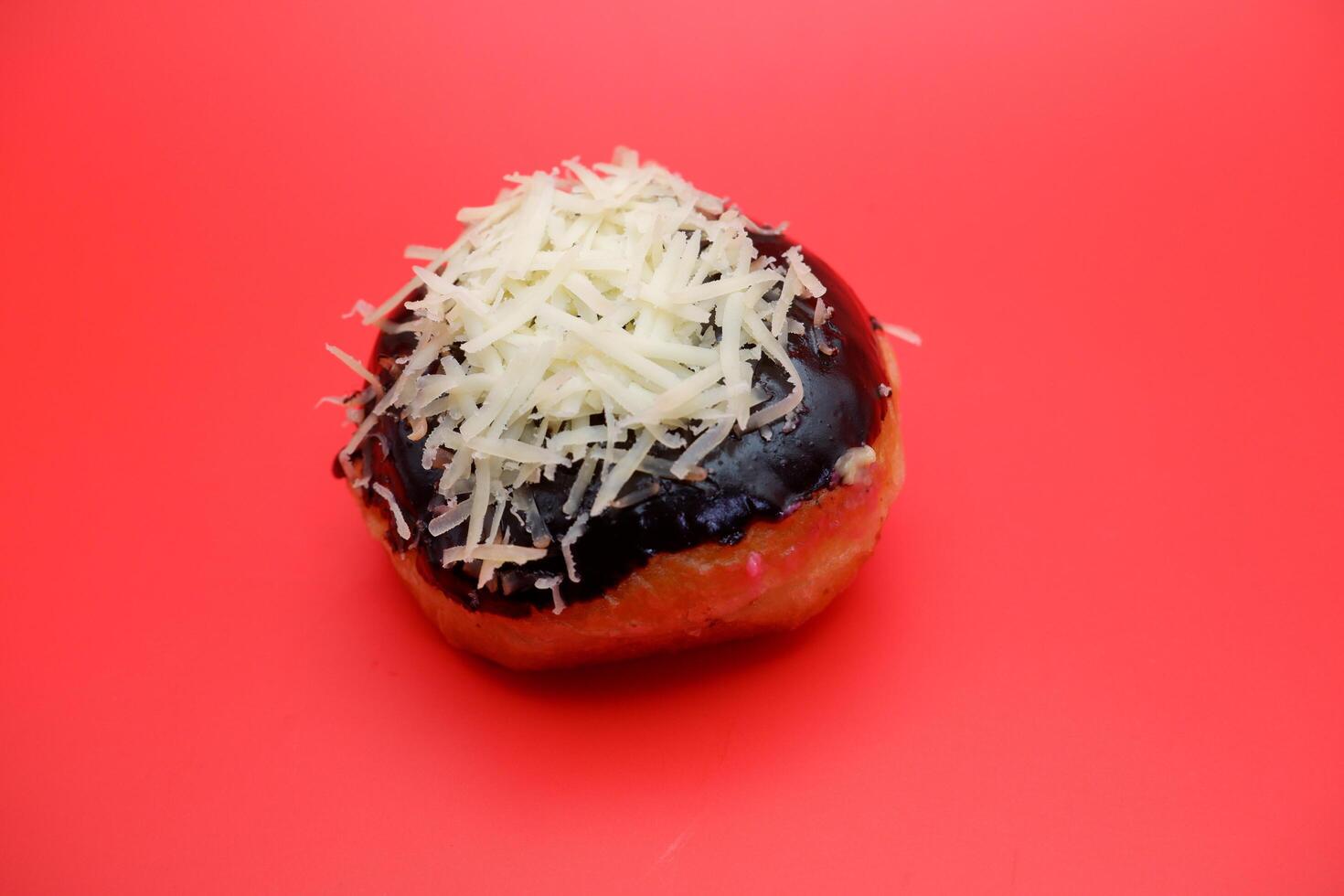 Donut cake with chocolate topping and grated cheese isolated on red background. photo