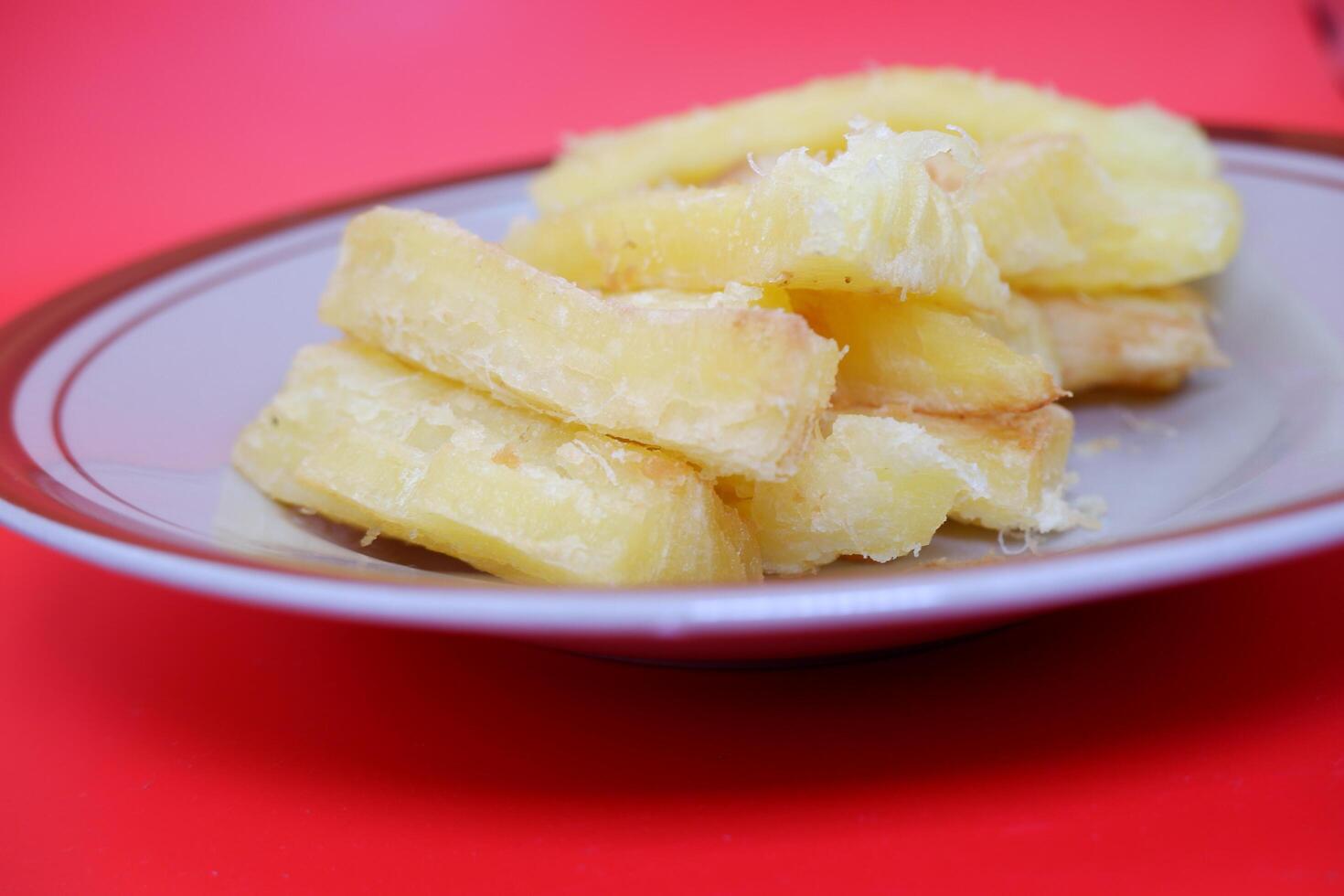 Fried cassava served on a plate. Fried cassava dish isolated on a red background. photo