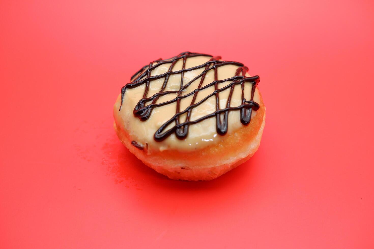donut cake with white chocolate glaze topping and chocolate spread in zigzag pattern. donut cake isolated on red background. photo