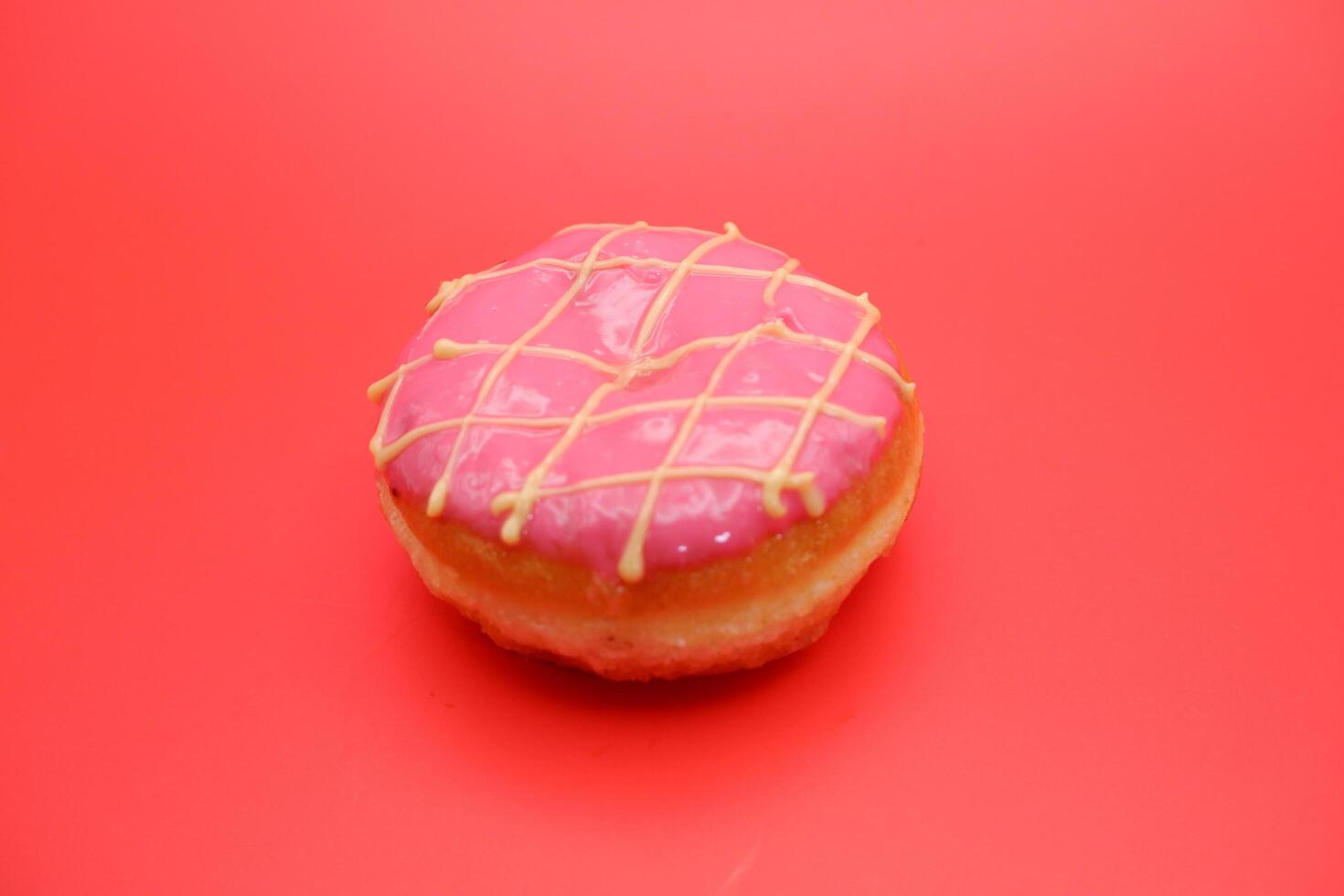 donut cake with pink chocolate glaze and white chocolate smeared in zigzag. donut cake isolated on red background. photo