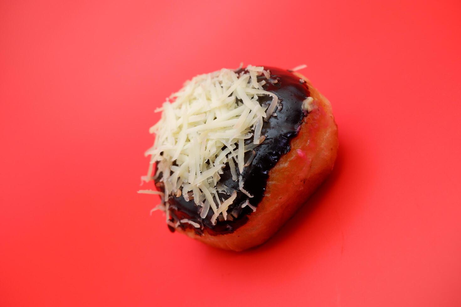 Donut cake with chocolate topping and grated cheese isolated on red background. photo