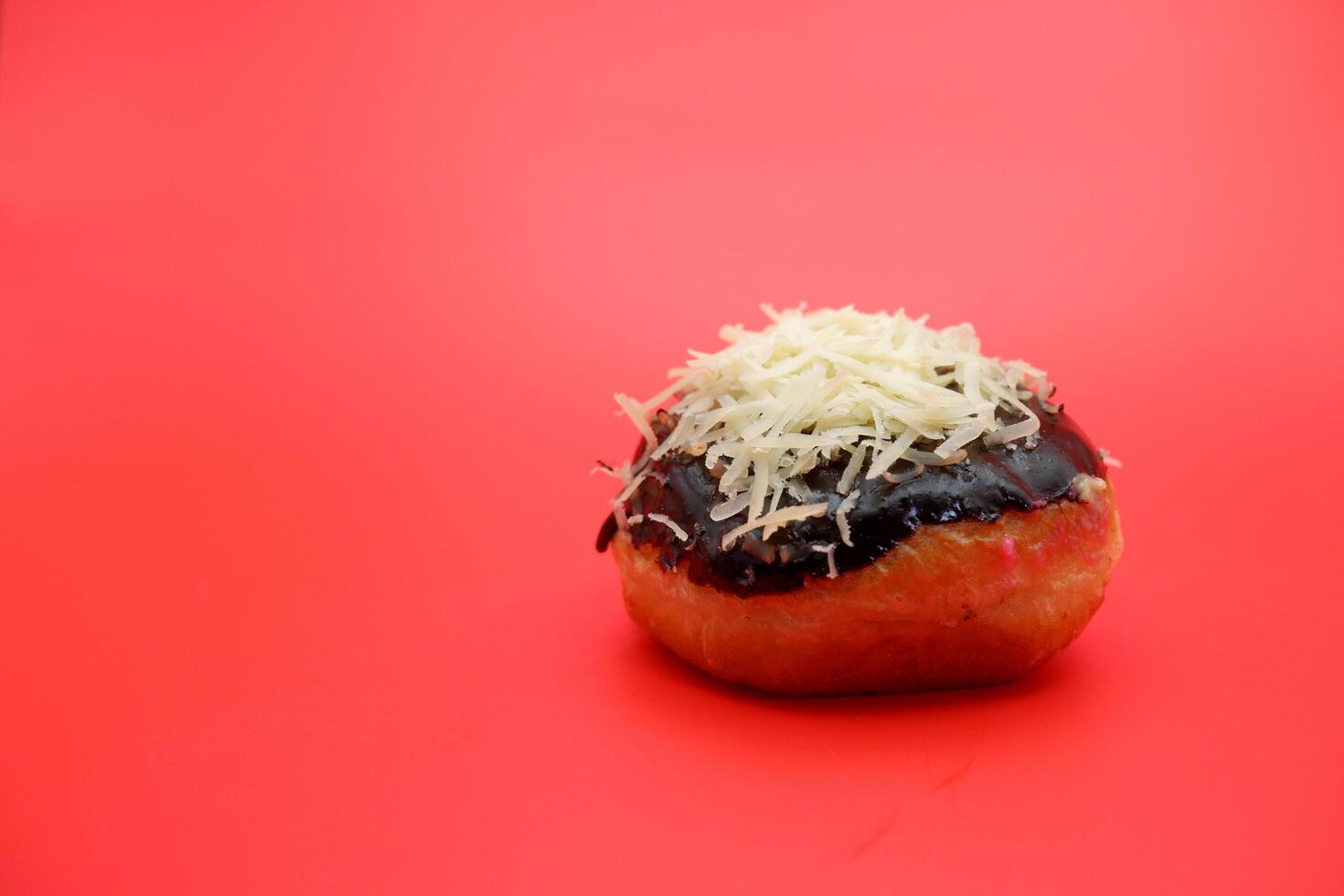 Donut cake with chocolate topping and grated cheese isolated on red background. photo