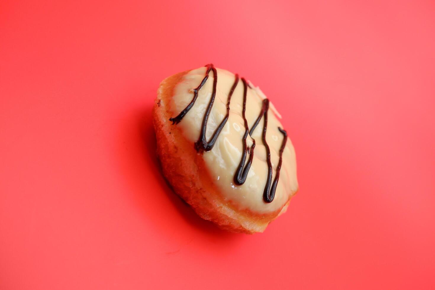 donut cake with white chocolate glaze topping and chocolate spread in zigzag pattern. donut cake isolated on red background. photo