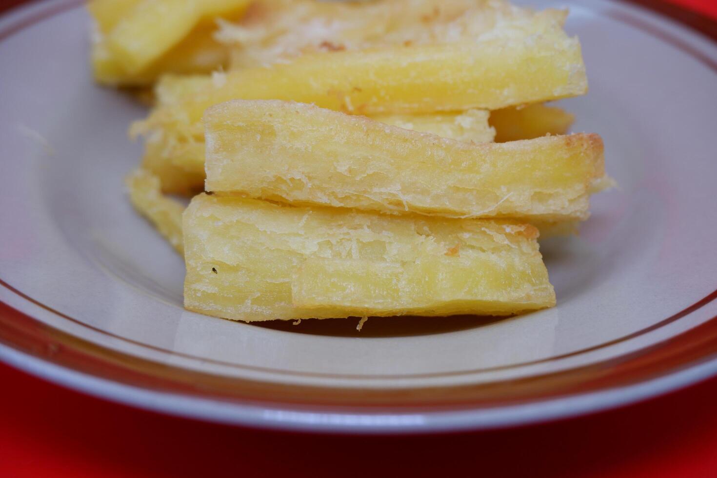 Fried cassava served on a plate. Fried cassava dish isolated on a red background. photo