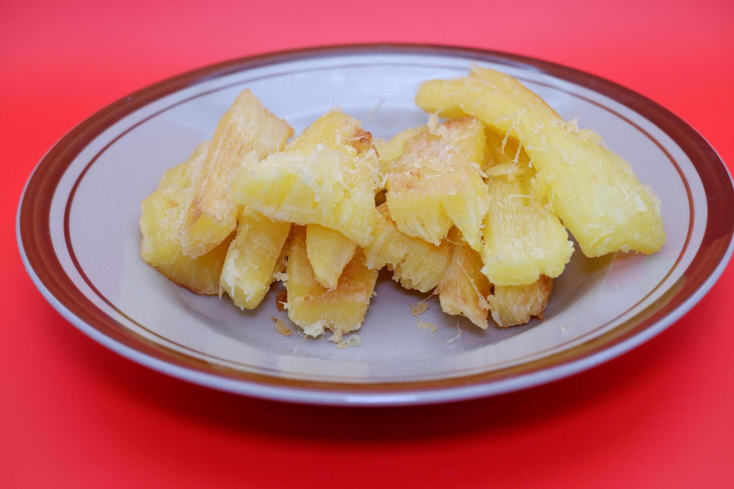 Fried cassava served on a plate. Fried cassava dish isolated on a red background. photo