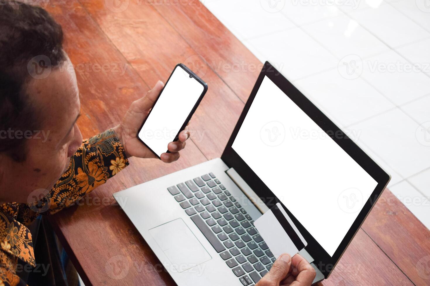 Top view Old man doing financial transaction with the white blank credit card, smart phone and laptop in living room, daily financial activity photo