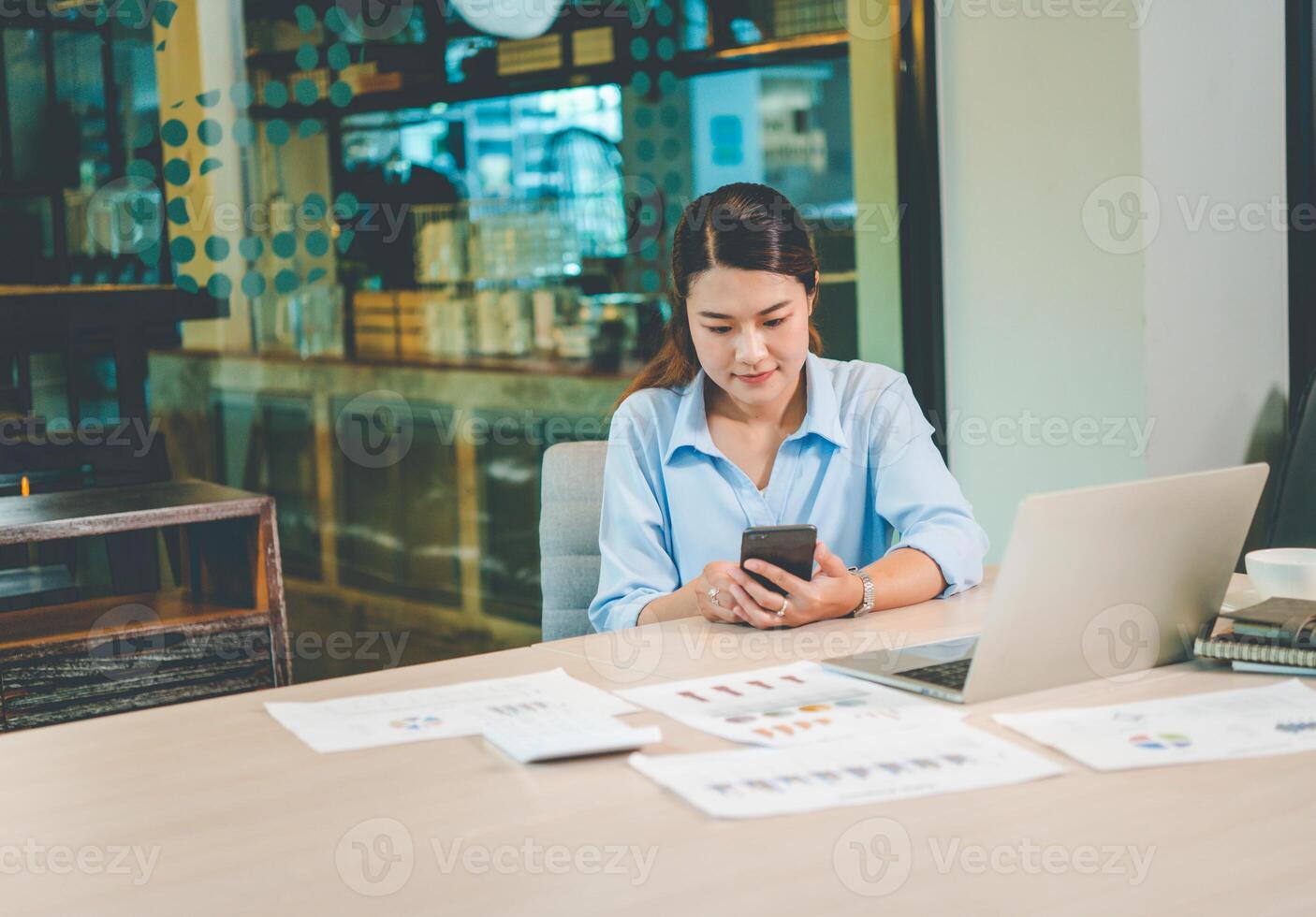 Business asian woman sitting at her desk with laptop using mobile phone during checking an email or social media on internet. photo