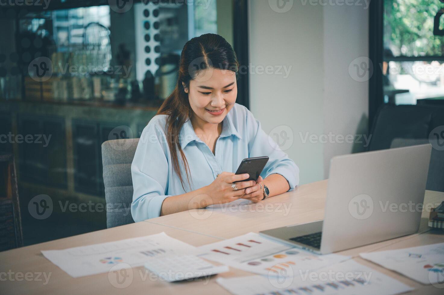 Business asian woman sitting at her desk with laptop using mobile phone during checking an email or social media on internet. photo