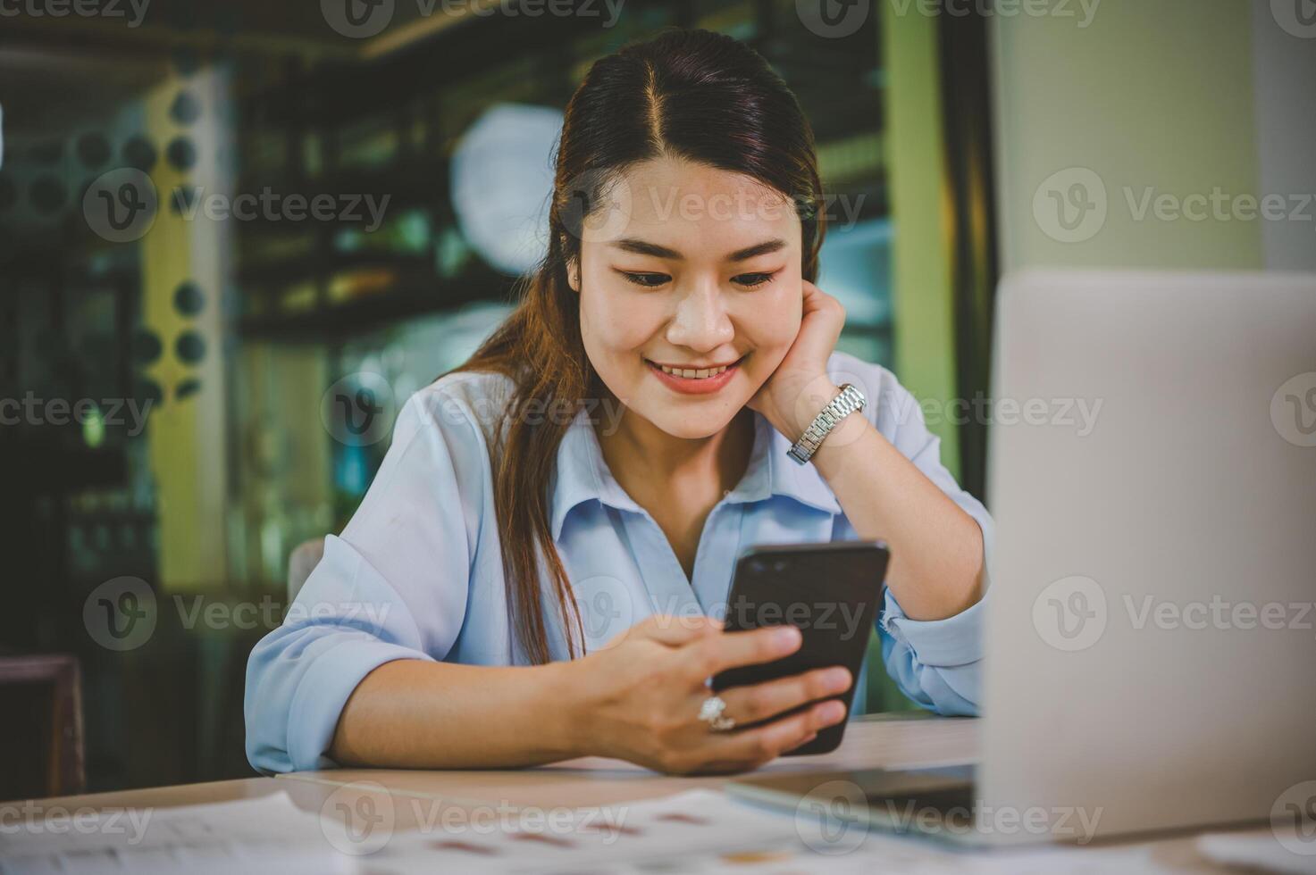 Business asian woman sitting at her desk with laptop using mobile phone during checking an email or social media on internet. photo