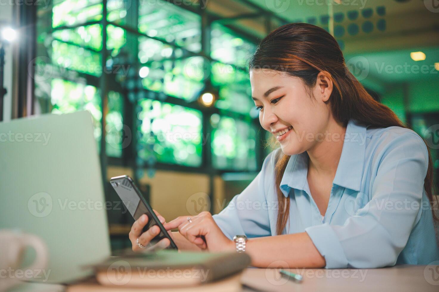 Business asian woman sitting at her desk with laptop using mobile phone during checking an email or social media on internet. photo