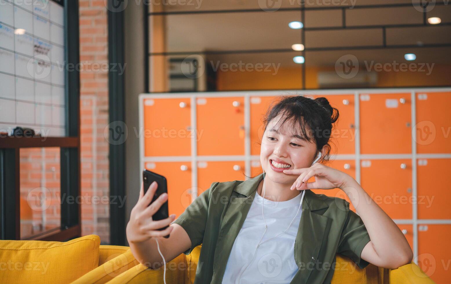 Smiling young asian woman using mobile phone checking social media,app playing game, shopping online, ordering delivery relax while sitting on a couch at cafe with laptop computer photo