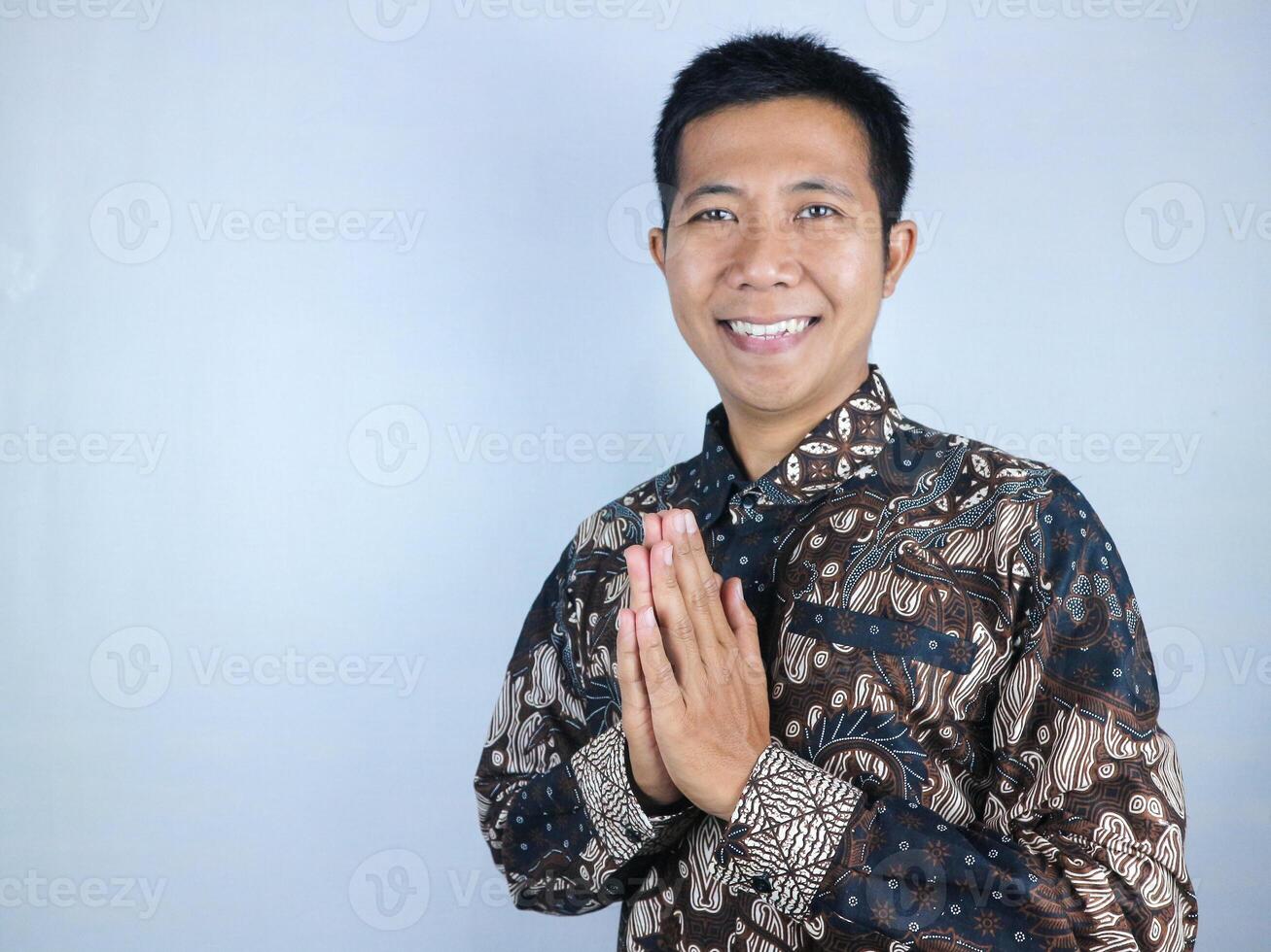 Smiling face ecpression of asian man wearing batik clothes looking at the camera doing greeting pose photo