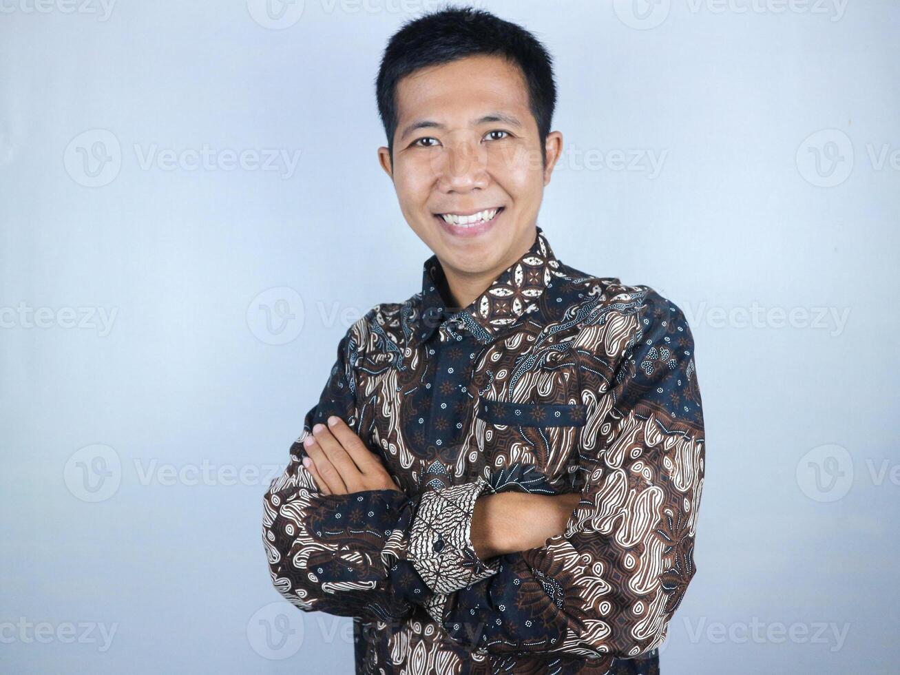 Smiling face ecpression of asian man wearing batik clothes looking at the camera while arm crossed photo