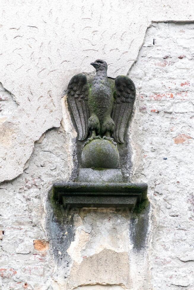 Statue of an eagle sitting on a pole behind a weathered wall photo