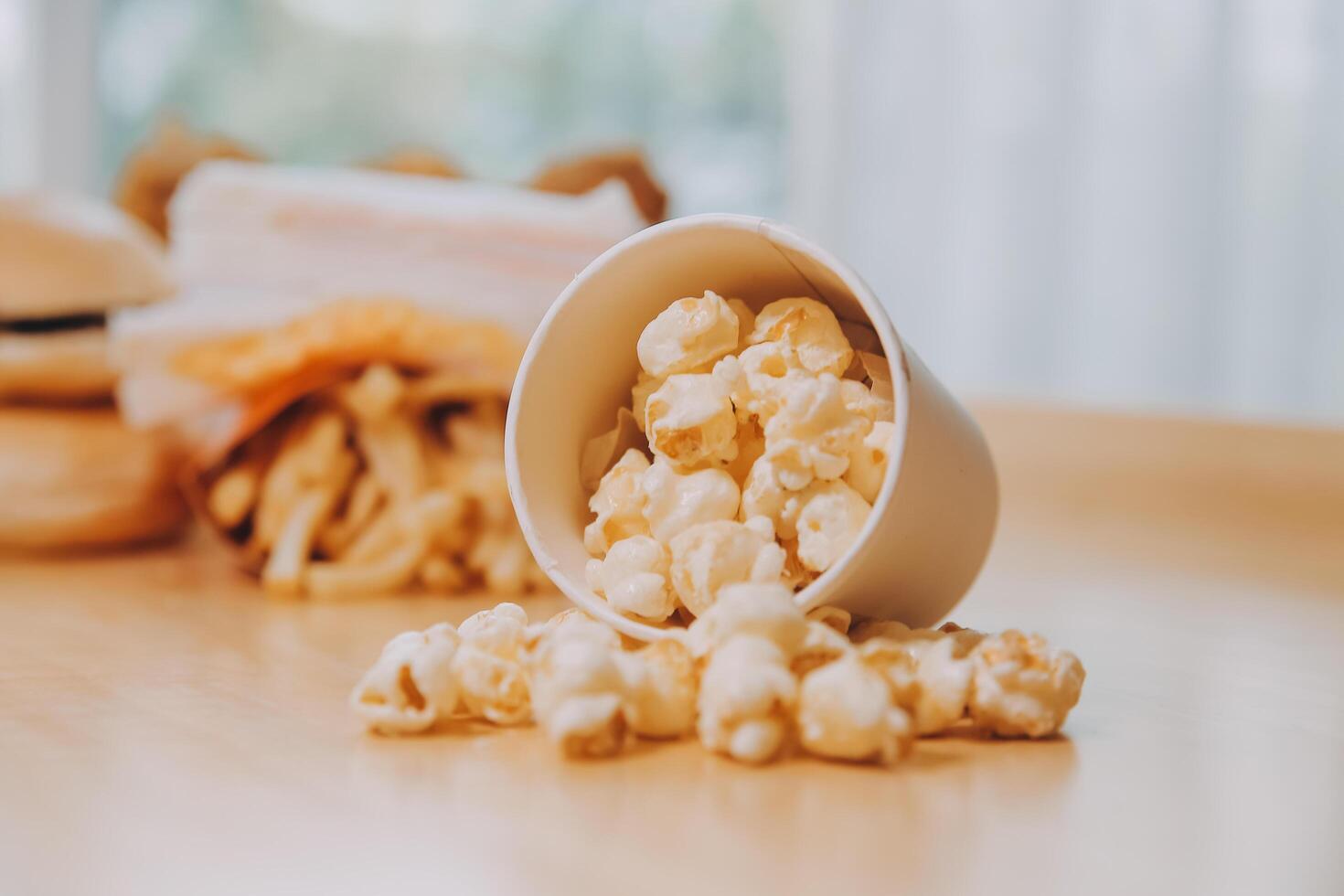 A bucket of popcorn, top-view, warm colors, light brown wooden background, flat lay, daylight macro close-up photo
