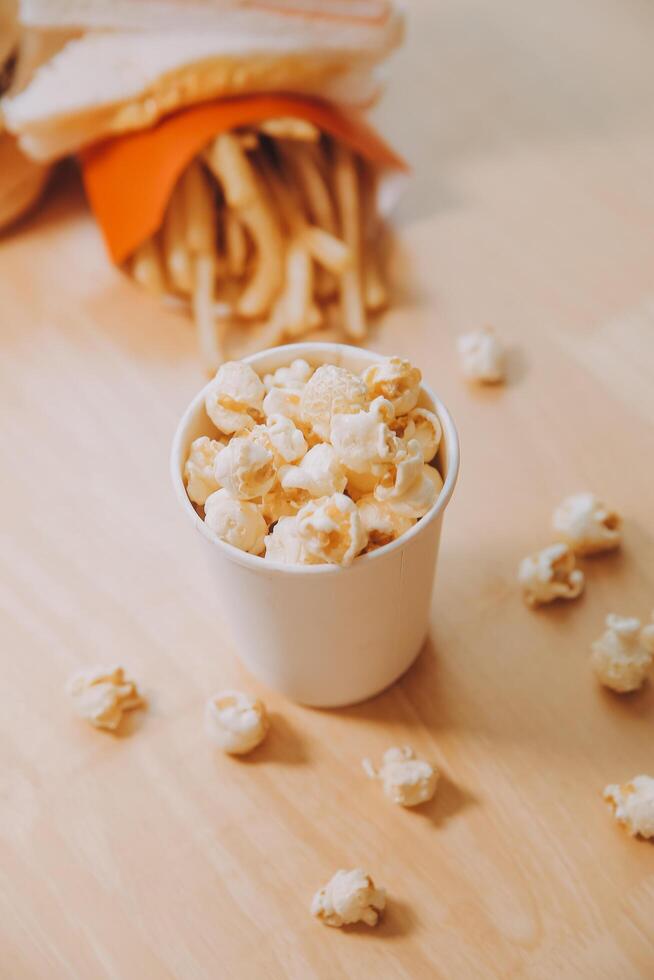 A bucket of popcorn, top-view, warm colors, light brown wooden background, flat lay, daylight macro close-up photo