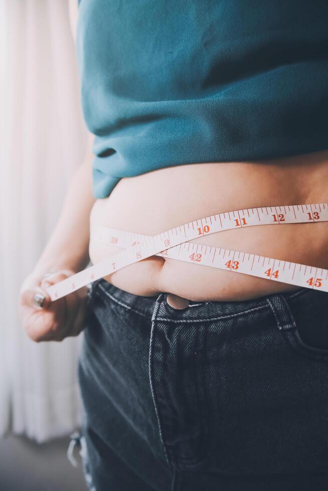 fat woman, fat belly, chubby, obese woman hand holding excessive belly fat with measure tape, woman diet lifestyle concept photo