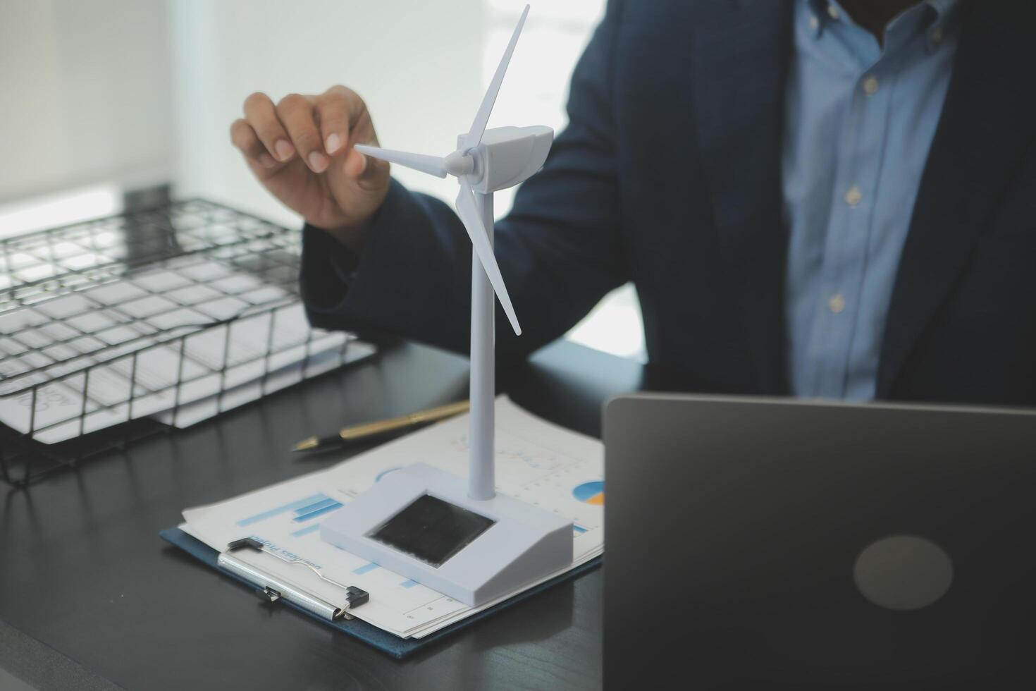 Shut of handsome business man working on new alternative energy development looking at a model of a wind turbine in modern startup. photo