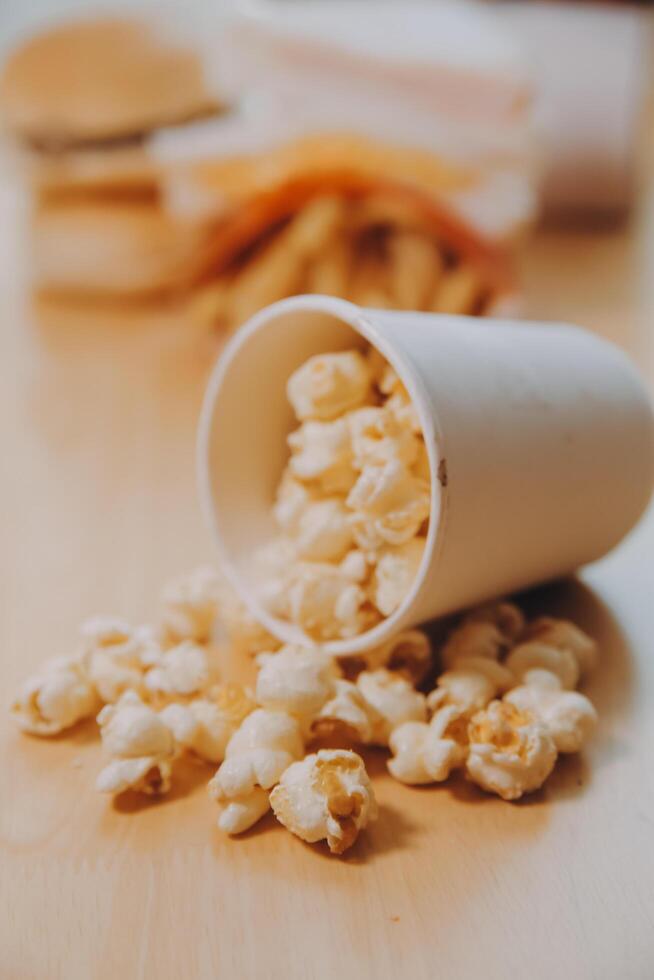 A bucket of popcorn, top-view, warm colors, light brown wooden background, flat lay, daylight macro close-up photo
